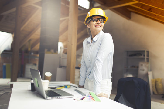 very pretty young female architect wearing yellow helmet is planning a loft in a house