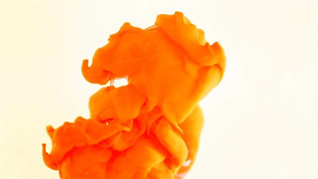 Macro shot of orange ink dropped into water, slow motion on white background 