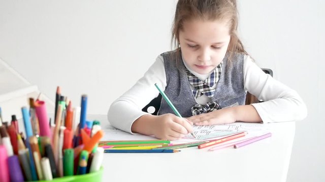 Little girl drawing a picture on white room. 7 years old girl drawing and coloring on a paper at home.