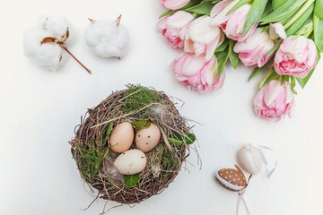 Fototapeta na wymiar Spring greeting card. Easter eggs in the nest with cotton and tulips on rustic wooden planks. Easter concept. Flat lay. Spring flowers tulips