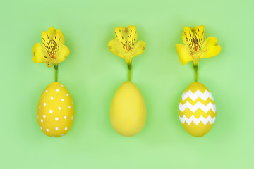 Happy Easter concept. Three yellow eggs with yellow flowers as symbol of spring lying in line on tint green background