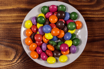 Saucer with colorful button shaped candies filled with chocolate on wooden table
