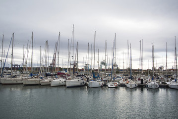 Fototapeta na wymiar Luxury Yachts And Boats In Valencia Port At Mediterranean Sea. Reflexion in the water. White yachts are in the Spanish port of Valencia in the beginning of spring. Cloudy sky.
