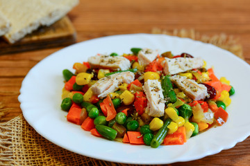 Chicken fillet and mixed vegetable stew on a white plate and a wooden table. Simple chicken vegetable stew. Stewed carrots, green beans, red beans, peas, corn, pepper and onions with chicken