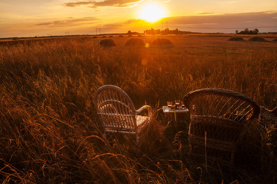 Two wicker chairs and a tray with glasses of wine amid the fields at sunset. Beautiful countryside. The expanse of fields rest on a farm, outside the city.
