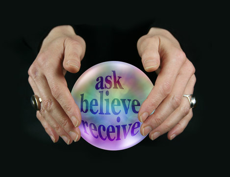 Crystal Ball says Ask Believe Receive  - female fortune tellers hands hovering around a crystal ball containing rainbow colored words ASK BELIEVE RECEIVE on black background
