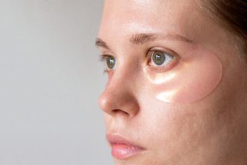 Girl uses pink hydrogel patches under her eyes. Cosmetology, self-care. Macro.