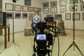 TV shooting at the Museum. LCD monitor on the camcorder. The girl in front of the camera. A record of the interview. Filming equipment and lighting equipment.