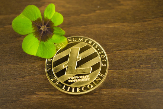 One litcoin with four-leaf clover on wooden background
