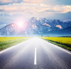 Old highway against mountains and a cloudy sky at the sunset