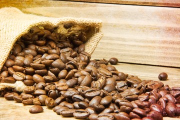 I close up of a burlap bag of coffee beans spilled onto a wood table with the focus on the beans closest to the burlap bag and a texture applied to the edges of the image.