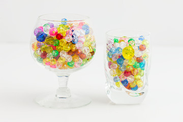 Two glasses of multi colored beads of varying sizes used to create jewelry