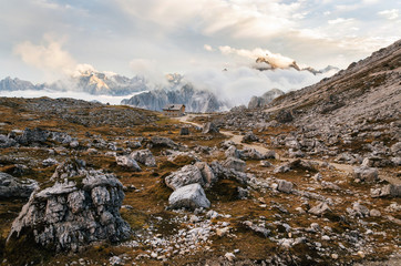 Fototapeta na wymiar Dolomites Alps rocky mountain range and Rifugio Locatelli at sunset with cloud drift, Tre Cime di Lavaredo, Italy
