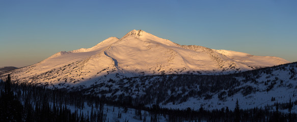 Winter mountain landscape with the top mountains lit by sunlight. Panoramic photo.