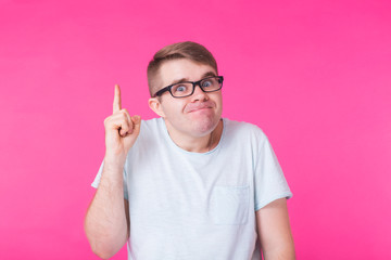 Portrait young man with glasses has an idea, pointing with finger up on pink background.