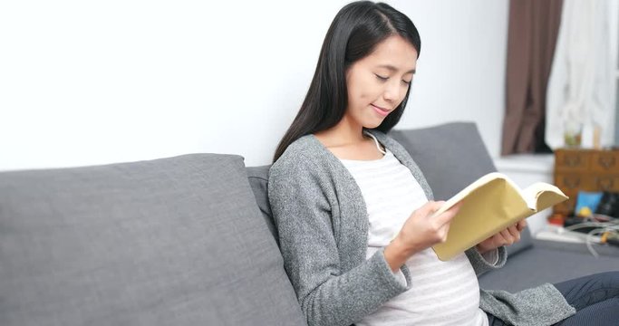Pregnant woman reading book and sitting on sofa