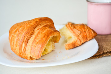 Close up of breakfast, cup of coffee and big tasty croissant on white plate on white table.