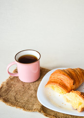 Close up of breakfast, cup of coffee and big tasty croissant on white plate on white table.