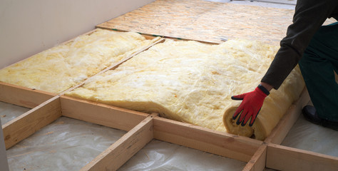Work composed of mineral wool insulation in the floor, floor heating insulation , warm house, eco-friendly insulation, a builder at work - obrazy, fototapety, plakaty