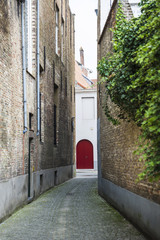 Narrow street with a red door of Bruges, Belgium
