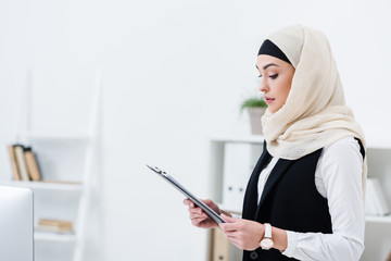 side view of muslim businesswoman in hijab with folder in hands in office