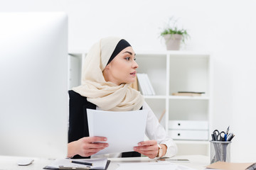 arabic businesswoman with papers in hands looking away at workplace