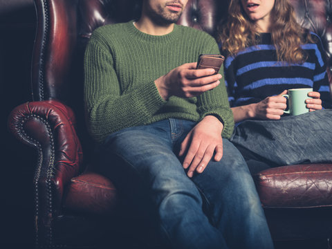 Man on sofa showing woman his phone