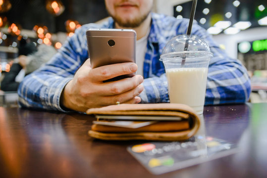 man searfing phone on background wallet with cup of milk shake on the table