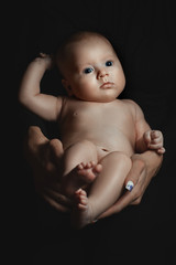 Portrait of a baby in the dark. Female hands hold the child