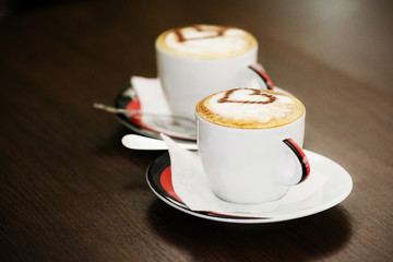 Two cups of coffee with heart pattern in a white cups on wooden background. Love concept.