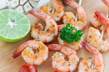 Skewers shrimp barbecue served on wood cutting board with lemon or lime in close up view. Delicious grilled prawn with spices for snacks in party. Homemade food concept of seafood menu.