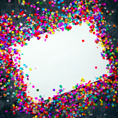 White sheet of paper in frame made of colorful confetti on black textured background.