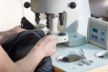 Closeup of a hand of a seamstress working on a machine for installing buttons on clothes.