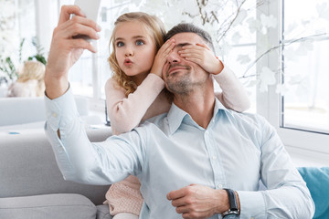daughter covering eyes of father and grimacing while they taking selfie
