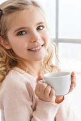 close-up portrait of happy little child drinking tea and looking at camera