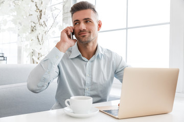 handsome businessman working with laptop and talking by phone at cafe