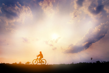 Silhouette of cyclist ride bicycle on sunset background. A man Ride on bike on the road with beautiful colorful sky. Sport and active life concept.