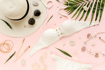 Feminine white swimsuit beach accessories, tropical palm leaf branches on pink background. Travel vacation concept. Summer background. Road frame set. Traveler accessories. Flat lay, top view. 
