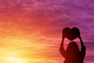 Silhouette of a woman holding a heart shape look at the sky sunset background - Powered by Adobe