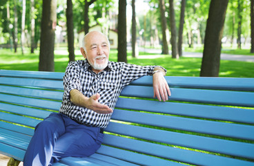 Fototapeta premium Smiling senior man sitting on the bench in park