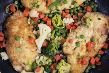 fried chicken fillet with spices in a frying pan and vegetables
