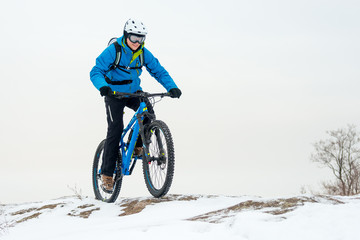 Obraz premium Cyclist in Blue Riding Mountain Bike on Rocky Winter Hill Covered with Snow. Extreme Sport and Enduro Biking Concept.