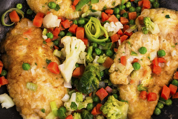 fried chicken fillet with spices in a frying pan and vegetables