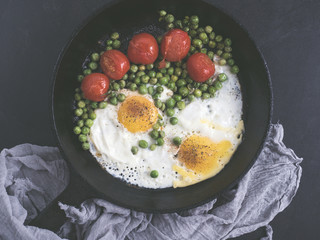 Fried eggs with tomatoes and green peas cooked on a beautiful, vintage, cast-iron frying pan