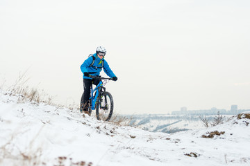Fototapeta premium Cyclist in Blue Riding Mountain Bike on Rocky Winter Hill Covered with Snow. Extreme Sport and Enduro Biking Concept.