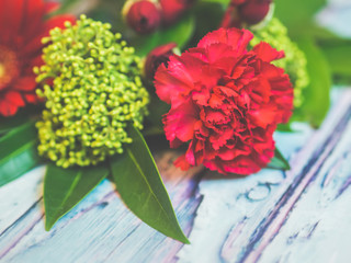 A bouquet of red and green flowers lying on a wooden table against soft-focused background.