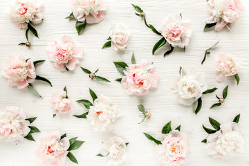 Texture made of pink and beige peony buds, branches and leaves isolated on white wooden background. The apartment lay, top view.