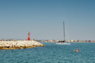 Summer. Italy. Rimini. Beach. Rocky shore, blue sea, a man in a kayak, a white yacht with passengers, a clear blue sky