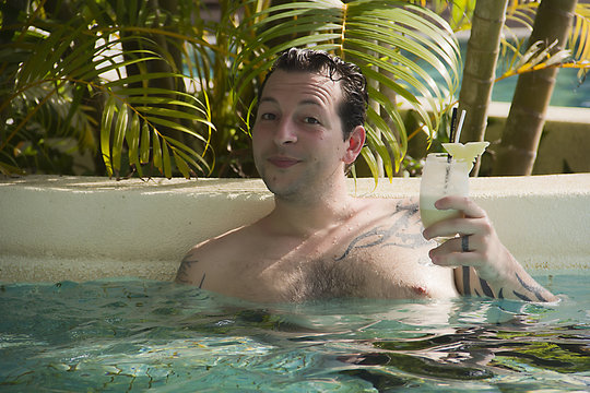 zufriedener Mann mit Cocktail im Pool
