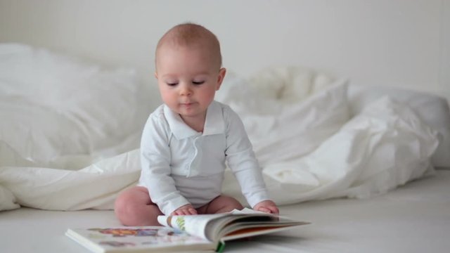 Little baby boy, looking at cook with colorful pictures at home, sitting in bed